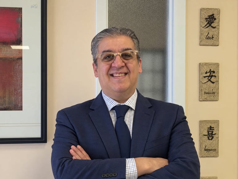 Professional man in navy blazer and tie, arms crossed, smiling in an office with Asian calligraphy artwork on the wall